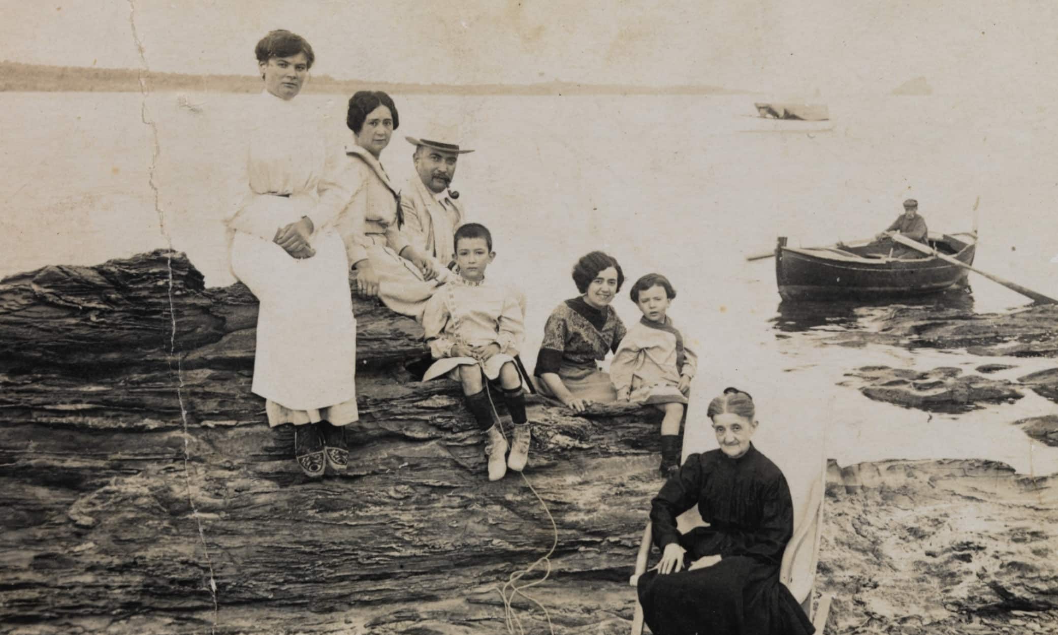 The Dalí family posing by the sea in Cadaqués, early 20th century, with a fisherman in a rowing boat on La Costa Brava.