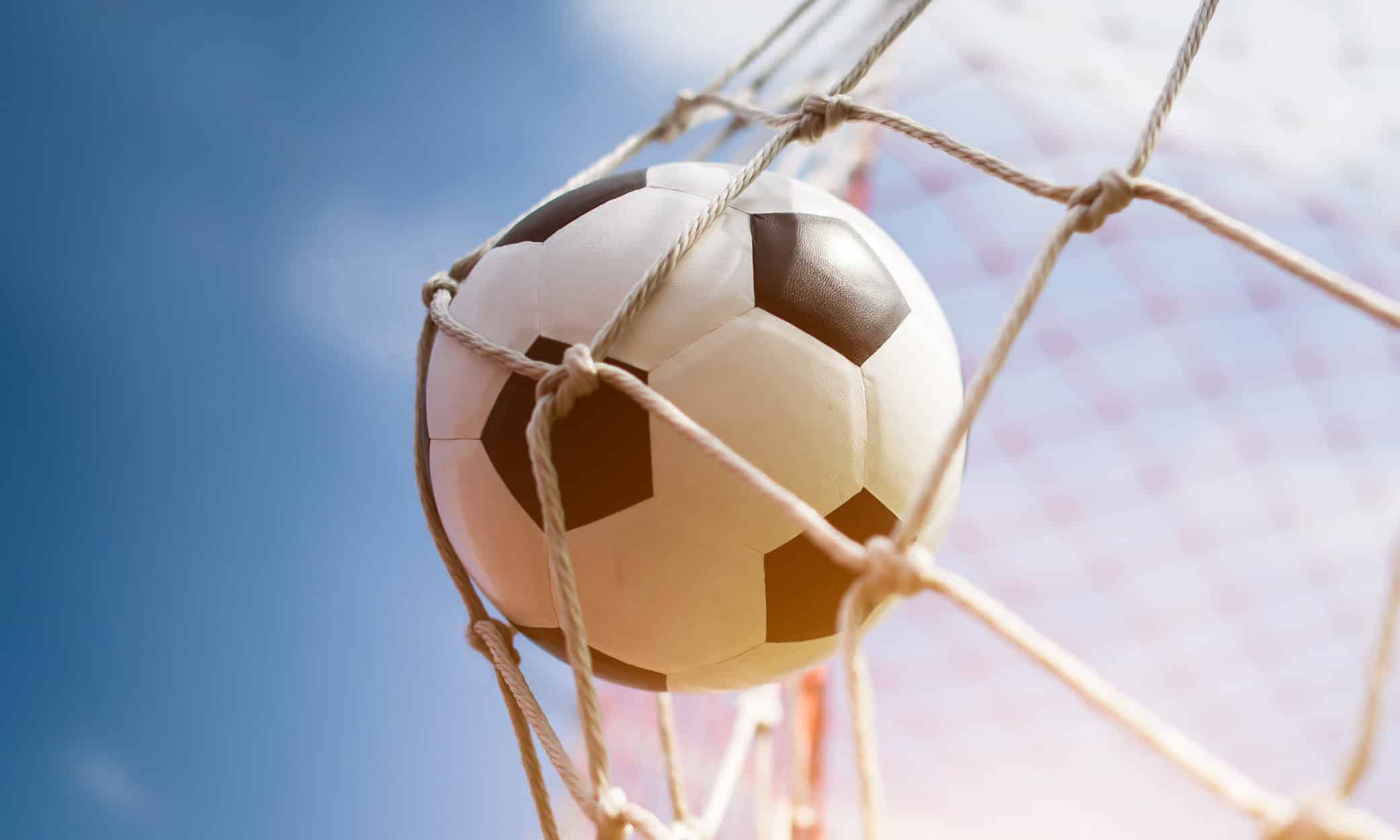 A classic black and white football caught in the net during a sunny day game.