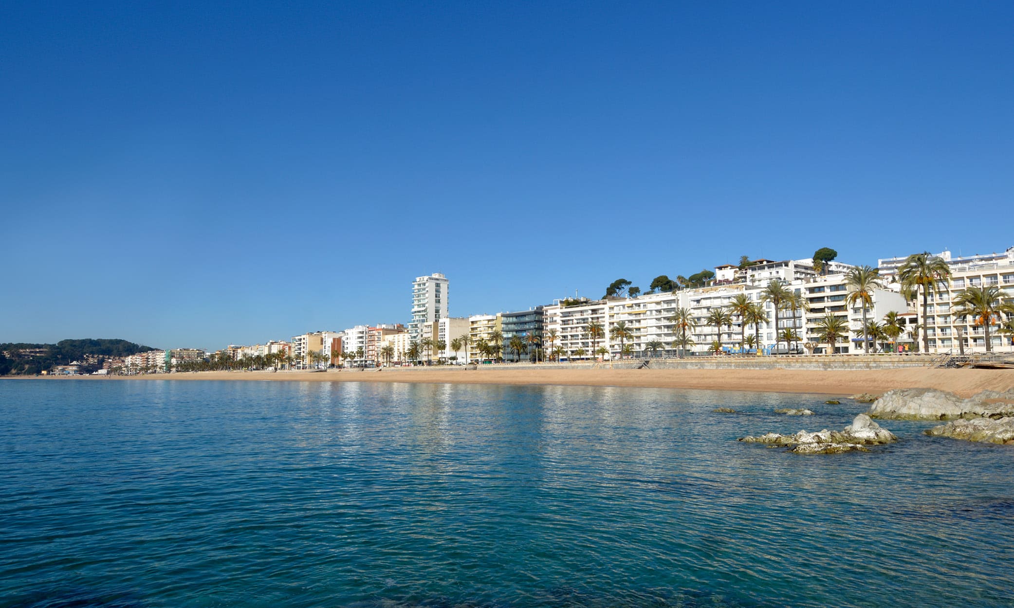 View of Lloret de Mar’s famous seafront with its sandy beach, palm-lined promenade, and Mediterranean waters.